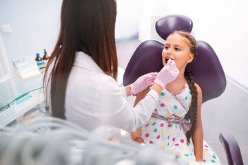 Little girl visiting dentists. Pretty girl opening his mouth wide during treating her teeth by the dentist.  Early prevention, oral hygiene and milk teeth care.