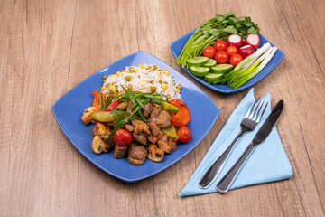 Delicious dinner. Fried chicken fillet with rice garnish and fied vegetables. Fresh vegetables served in blue plate on wooden table.