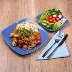 Delicious dinner. Fried chicken fillet with rice garnish and fied vegetables. Fresh vegetables served in blue plate on wooden table. Square format, copy space.