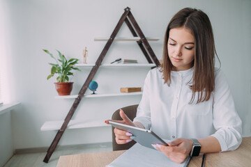 Young attractive business woman in a white shirt working on a tablet at her desk, Concept of business woman accountant with bills and paper folders in the office.
