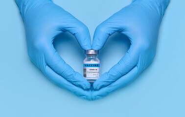 Doctor's hands in protective medical gloves hold a bottle of coronavirus vaccine in a heart-shaped gesture on a blue background. Vaccination. Immunization. Fighting the pandemic. Banner. Copy space