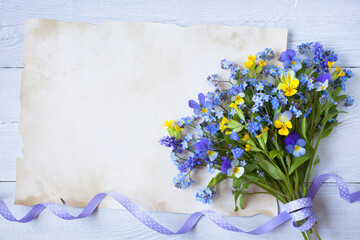 Bouquet of forget-me-not flowers, pansies, primroses, muscari and paper for congratulation text on a white wooden background.