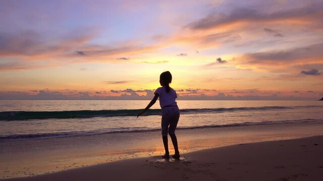 Silhouette of the young girl jumping on the beach and raise their hands up on the beach at sunset Amazing light sunset or sunrise sky Baby girl happy and relax watching sea