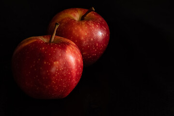 Fototapeta na wymiar Two ripe fresh red apples with water drops on glossy peel on black background