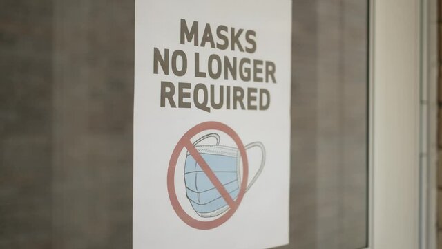 A small business owner puts a "Masks Not Required" sign on his front door. Shot at 60fps for optional slow motion use.  	