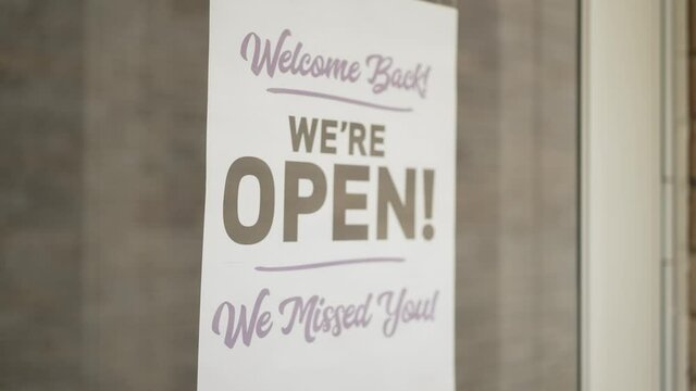 A small business owner puts a "Welcome Back We Missed You" open sign on his front door. Shot at 60fps for optional slow motion use.  	