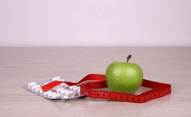 Green apple, red measuring tape and pills in a package. Healthy food concept. Diet for health and a good figure