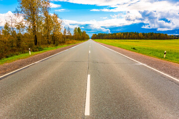 Fototapeta premium Autumn sky in the clouds lit by the sun over the empty road and boundless fields of the forest. Wide angle view