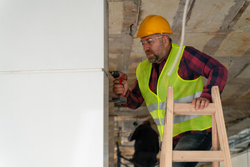 Repairman on a ladder drilling with a machine into a ceiling