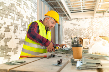 Builder in working uniform with protective helmet standing with instruments at the construction site indoors