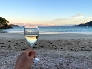 Hand holding glass of wine at the beach with ocean view, Matauri Bay, New Zealand