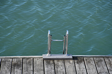 Silver metal ladder leading into turquoise water from a wooden deck
