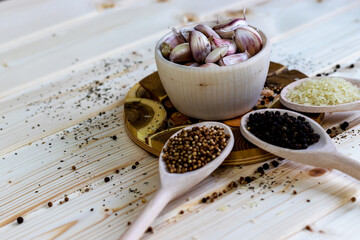 Three wooden spoons with spices, coriander, peppercorns, rice and a bowl of garlic cloves on a wooden background. Rustic concept and copy space