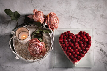 Drei Rosen in Alt Rose' Farben, ein Kerzenständer mit Perlen und Himbeeren Torte im Herz Form liegen auf dem Marmorhintergrund auf dem weißen Tablett aus Metall. Vintage, Hintergrund. Stillleben