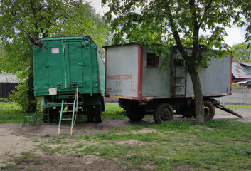 Fototapeta na wymiar Two old green and gray trailers on wheels sit in dry grass next to a construction site. The inscription - no turns, no stops, no overtaking.