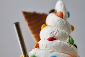 Sundae visto desde frente macro, con crema batida, rockets ,una bombilla y un trozo de cucurucho sobre un fondo blanco