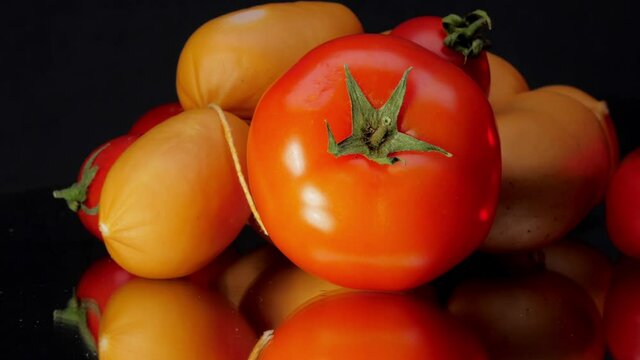 Cherry tomatoes and brown bangers bunch lie on black glass table reflecting on surface in kitchen close view
