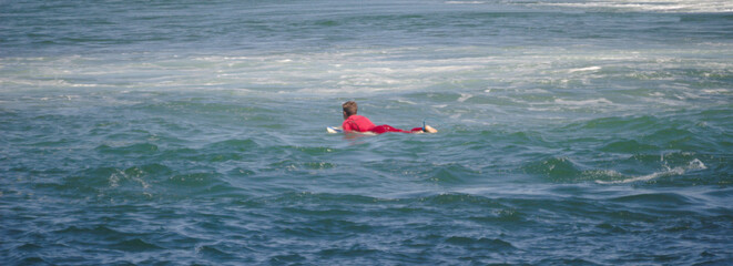 Surfista deitado em cima da praia a entrar no mar para apanhar uma onda - fato de neoprene vermelho - obrazy, fototapety, plakaty