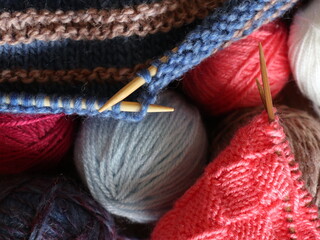 Close up multicolored knitting yarn balls and needles with knitting fabric. Handicraft concept.