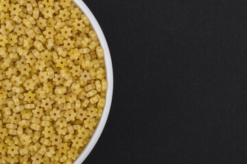 White glass bowl of stars shaped pasta. Isolated on a dark grey background.