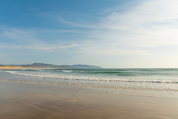 Blue transparent sky with lacy white clouds over the ocean. Mountains can be seen in the distance. Pastel shades. Beautiful nature. There is an empty space for your signature.