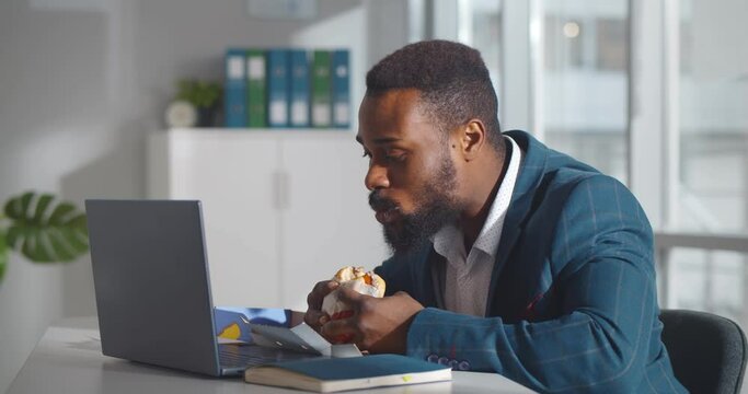 African male worker in office having fast food lunch at desk