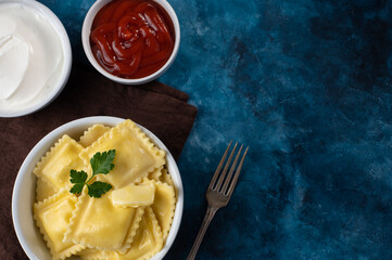 ravioli is tasty and healthy food. In the foreground is a plate with ravioli, butter and a piece of mint, next to it is a fork. In the background is a saucepan made of tomato sauce.