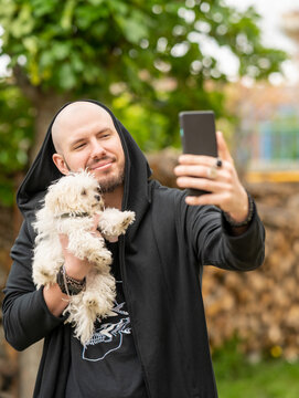 modelo masculino sonriente con cachorro de bichon maltes haci&eacute;ndose un selfie