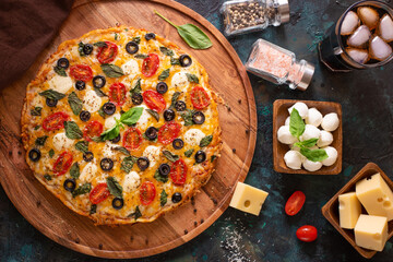 Pizza on a wooden platter and next to it - the ingredients that make up the pizza - cheese, tomatoes, mushrooms, seafood. Beautiful still life. Bright colors of the photo. View from above.
