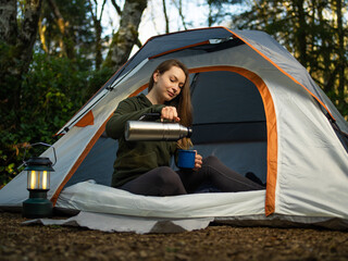 A woman is resting in a paddock in nature. Drinks tea from a thermos. Relaxation, rest, pacification. Forest. Silence, fresh air. The woman is calm and happy. Pastel shades.