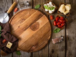 Preparing to cook pizza. Wooden table, cutting round brown board, rolling pin, tomatoes, mushrooms, herbs, cheese, Small details. Color image. No people.