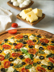 The photo shows a part of Italian pizza. Beautiful wooden stand. In the background, in a brown bowl, cheese and a tomato, then mushrooms. White background