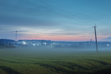 Field and lonely houses in the distance in the spring before dawn in the fog