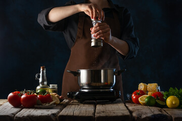 The cook prepares vegetable soup. Vegetarian food. In the photo, the chef adds spices to the soup. vegetables on the table. Bright colors. Dark background.Homemade food. Restaurant food.