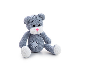 Grey knitted teddy bear toy with patch  sitting over white background with soft shadow