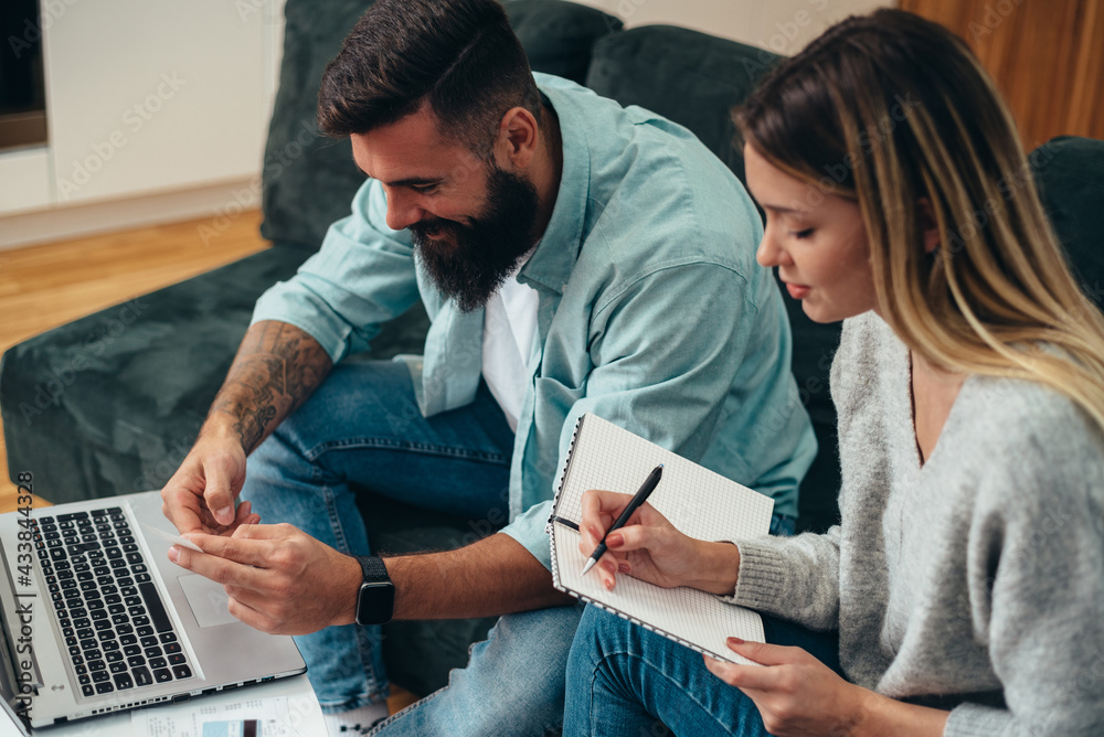 Wall mural Young beautiful couple using a laptop calculating their finances at home