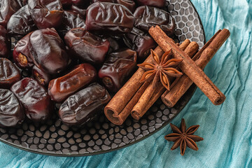 Delicious dried Iranian dates, few cinnamon sticks and star anise on a black ceramic plate over turquoise cloth. Sweet vegetarian healthy food ingredient. Ready to eat organic fruits and berries.