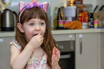 Baby Girl In A Kitchen Eating With A Spoon
