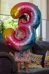 A Cute Baby Girl Holding A Number Three Balloon