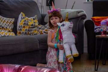 A Cute Baby Girl Sitting On The Floor With a Balloon And An Unicorn Pinata