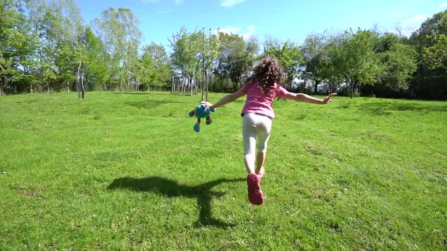 une fillette de dos , courant au ralenti avec une peluche &agrave; la main