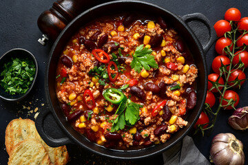 Chili con carne - traditional mexican minced meat and vegetables stew in tomato sauce in a cast iron pan . Top view with copy space.