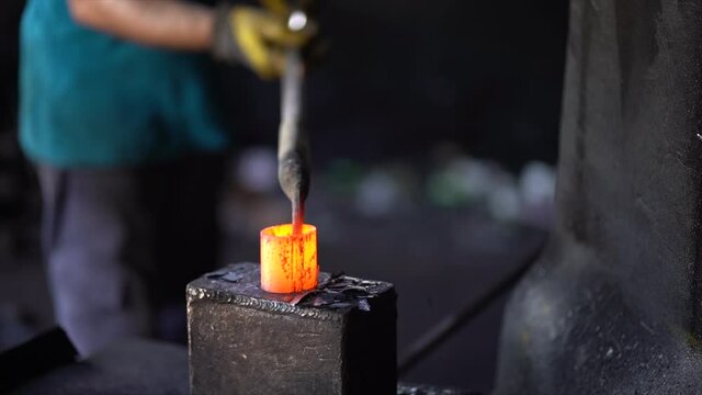 Worker forging metal in the workshop, with machine in slow motion