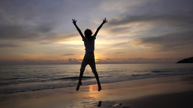 Silhouette of the young girl jumping on the beach and raise their hands up on the beach at sunset Amazing light sunset or sunrise sky Baby girl happy and relax watching sea in Slow motion