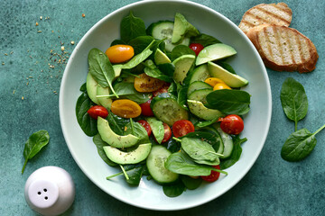 Fresh vegetables salad with spinach, avocado, cucumber and cherry tomatoes. Top view with copy space.