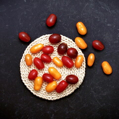 Plum Cherry On White Round Cutting Board. Assorted Plump Cherry Tomatoes On Wooden Cutting Board. Scattered Red, Yellow And Black Plum Cherry Tomato On Black Grunge Background.