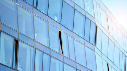 Modern glass building and rising sun. Glass facade on a bright sunny day with sunbeams in the blue sky. Economy, finances, business activity concept.  