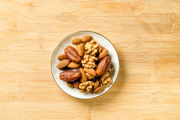 Raw almonds, organic pitted dates and walnut halves in a white porcelain saucer with a gold border on a wooden cutting board