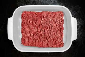 Raw Minced Meat in White Ceramic Dish Isolated On Black Background. Top View of Fresh Ground Beef Isolated on Black. Uncooked Minced Beef Meat.
