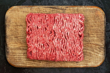 Cutting Board With Raw Minced Meat On Black Vintage Background. Top View Of Fresh Ground Beef Isolated On Black Background. Uncooked Minced Mixed Beef And Pork Meat On Old Cutting Board.